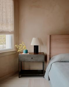 a bedroom with a bed, nightstand and lamp on the side table next to it