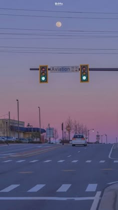 a traffic light hanging over a street next to a parking lot at dusk with the moon in the sky