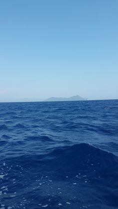 the ocean is very blue and clear with no waves on it, but there are mountains in the distance