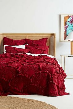 a bed with red comforter and pillows in a room next to pictures on the wall