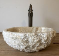 a stone bowl shaped sink sitting on top of a wooden table next to a faucet