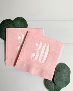 two pink napkins with the number 30 printed on them and green leaves around it