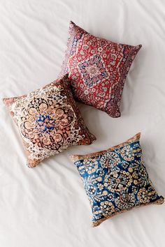 three pillows on a bed with white sheets and blue, red, and orange designs