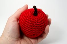 a crocheted red apple in someone's hand on a white background,