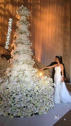 a bride and groom standing in front of a wedding cake with white flowers on it