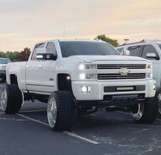 a white truck parked in a parking lot next to other trucks with large tires on them