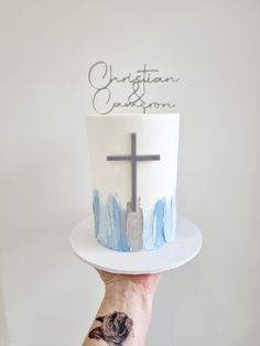 a person holding up a cake with a cross on it and the word christian written on top