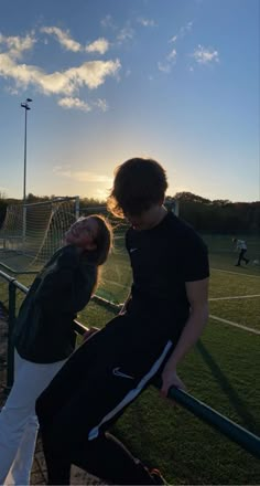 two people leaning against a rail on a soccer field