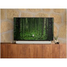 a flat screen tv sitting on top of a wooden entertainment center next to a stone wall