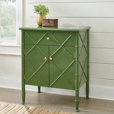 a green cabinet with gold knobs and a plant on top in front of a window