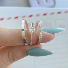 a woman's hand holding three rings with diamonds on them, and one ring has a diamond in the middle