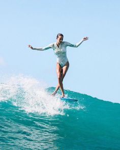 a woman riding a surfboard on top of a wave in the ocean with her arms outstretched