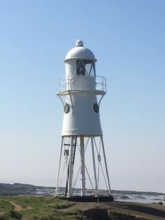 a white lighthouse sitting on top of a lush green field next to the ocean with people walking around it