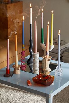 there are many candles on the table with different colors and shapes in them, all lit up