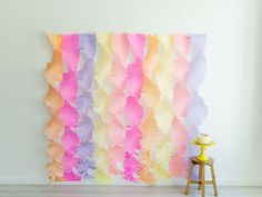 a wall hanging made out of colorful feathers on a white wall next to a stool