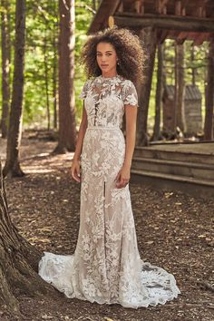 a woman standing in the woods wearing a wedding dress with an open back and short sleeves