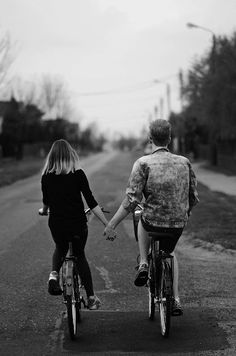 a man and woman riding bikes down a road holding hands with the other person's hand