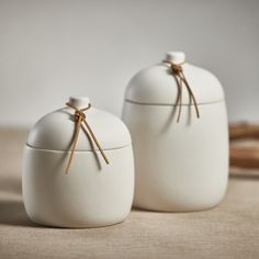 two white jars with wooden sticks sticking out of them on a beige tableclothed surface