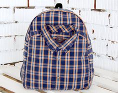 a blue and yellow plaid backpack sitting on top of a wooden bench in front of a white brick wall