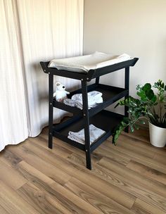 a baby changing table in the corner of a room next to a potted plant