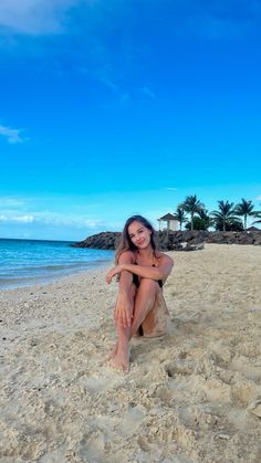 a woman sitting on top of a sandy beach next to the ocean and palm trees