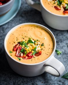 two white bowls filled with soup and garnished with fresh vegetables on the side