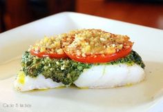 a white plate topped with fish covered in pesto and tomato slices on top of it