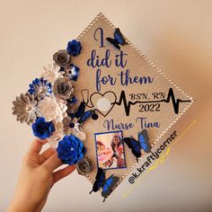 a graduation cap decorated with blue flowers and butterflies is held up by someone's hand