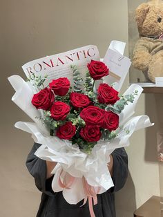 a woman holding a bouquet of red roses in front of a teddy bear and book