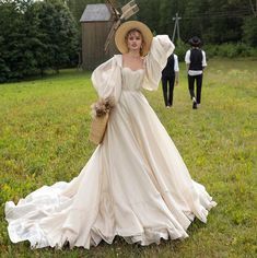 a woman in a white dress and hat walking across a grass covered field next to a man