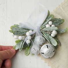 a hand holding a silver bell with holly and white balls on it's side