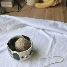 a bowl with yarn in it sitting on a table next to bananas and other items