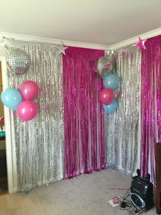 balloons and streamers are hanging from the ceiling in front of curtained walls with pink tinsel