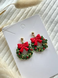 pair of christmas wreath earrings with red bows and holly leaves on white carded background