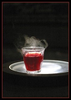 a glass filled with red liquid sitting on top of a white plate covered in steam