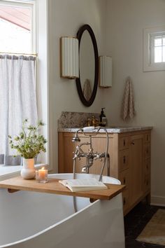 a bath tub sitting next to a window with a mirror on the wall above it