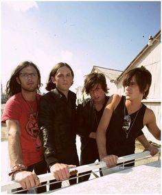 four young men standing next to each other in front of a fence and building with a sky background