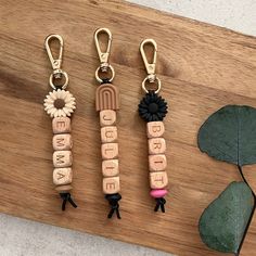 three wooden keychains with flowers and letters on them sitting next to a plant