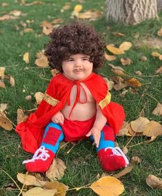 a baby doll sitting on the ground wearing a red cape and blue pants with yellow leaves around it