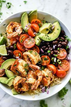 a white bowl filled with shrimp, black beans, tomatoes and avocado garnished with cilantro