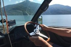 a man driving a truck down a road next to a lake with mountains in the background