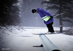 a man riding skis on top of a wooden log in the middle of a snow covered forest