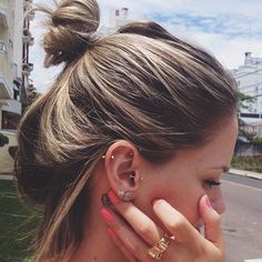 a woman with ear piercings on her ears and hand to her face, looking down the street