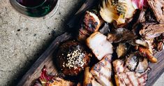 grilled meats and vegetables on a cutting board next to a cup of tea