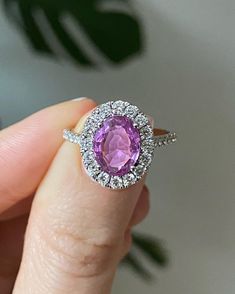 a close up of a person holding a ring with an oval shaped pink stone in it