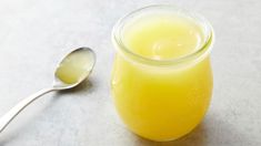 a glass jar filled with yellow liquid next to a spoon on a white counter top