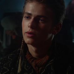 a young man with braids on his neck stares into the distance while standing in front of other people