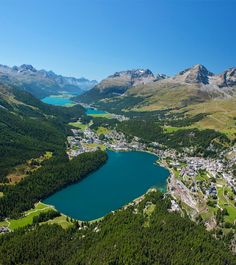 an aerial view of a town and lake surrounded by mountains with blue water in the foreground