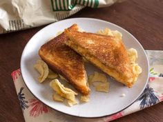 two grilled cheese sandwiches on a white plate with potato chips next to the bag