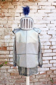 a mannequin wearing a jacket and hat made out of metal mesh with a blue pom - pom on top